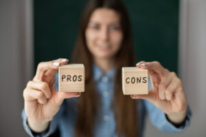 Person holding wooden blocks labeled 'Pros' and 'Cons,' symbolising the evaluation of positive and negative aspects.
